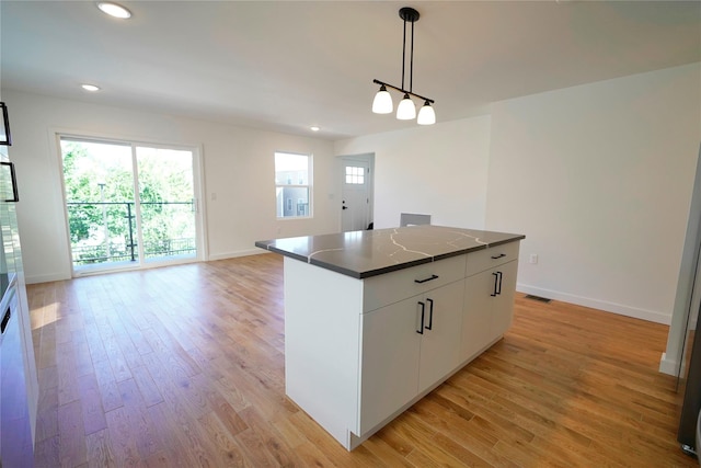 kitchen with dark countertops, a kitchen island, light wood finished floors, pendant lighting, and baseboards