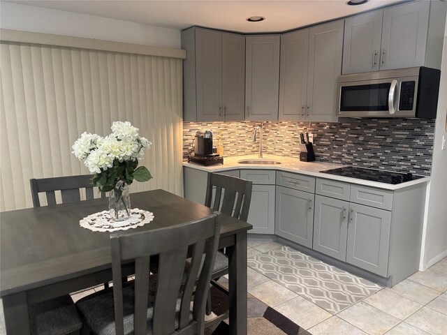 kitchen featuring stainless steel microwave, gray cabinetry, a sink, black electric cooktop, and backsplash
