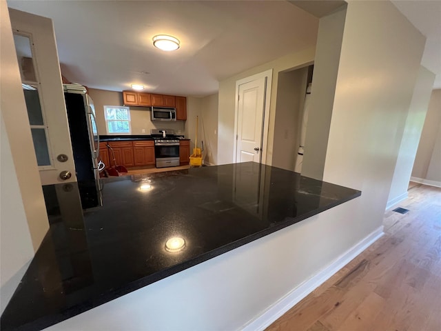 692 Burlingham Rd, Bloomingburg, NY 12721 - kitchen with stainless steel appliances, a peninsula, light wood-style flooring, brown cabinetry, and dark countertops
