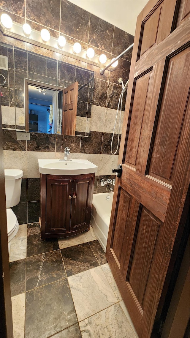 full bath with tile walls, toilet, vanity, and tub / shower combination