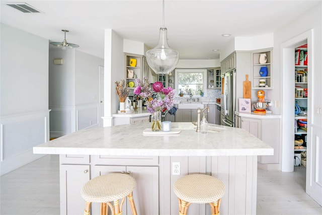 6 Beech Hollow Ct, Montauk, NY 11954 - kitchen featuring open shelves, a sink, a kitchen island with sink, stainless steel refrigerator, and light stone counters