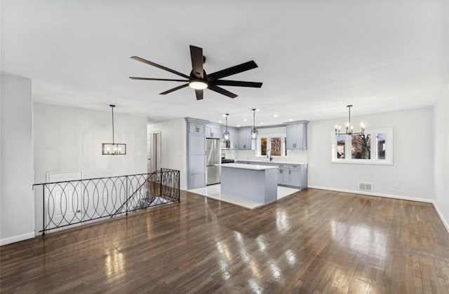 unfurnished living room featuring a chandelier, ceiling fan, wood finished floors, and baseboards