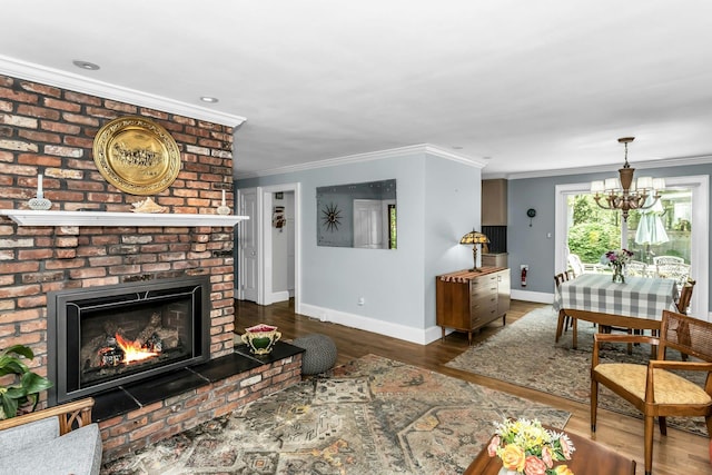 living room featuring baseboards, ornamental molding, wood finished floors, a chandelier, and a brick fireplace