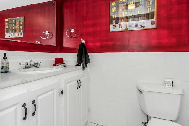 half bathroom with toilet, tile walls, vanity, and wainscoting