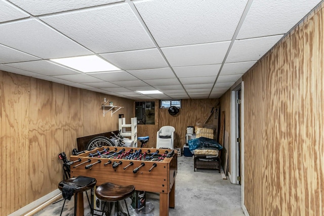 game room with wooden walls, a paneled ceiling, and concrete floors