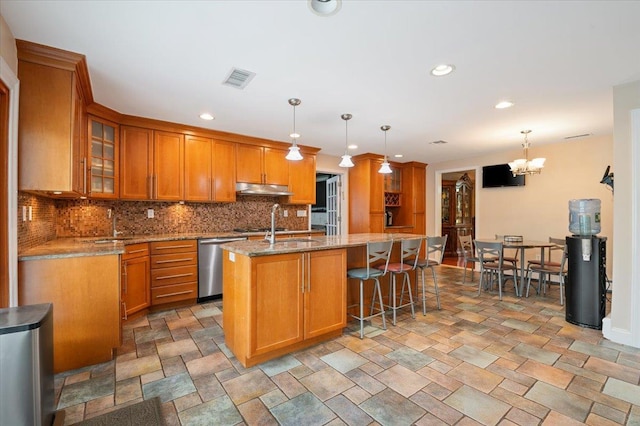 525 Green Pl, Woodmere, NY 11598 - kitchen with dishwasher, under cabinet range hood, a center island with sink, brown cabinets, and light stone countertops