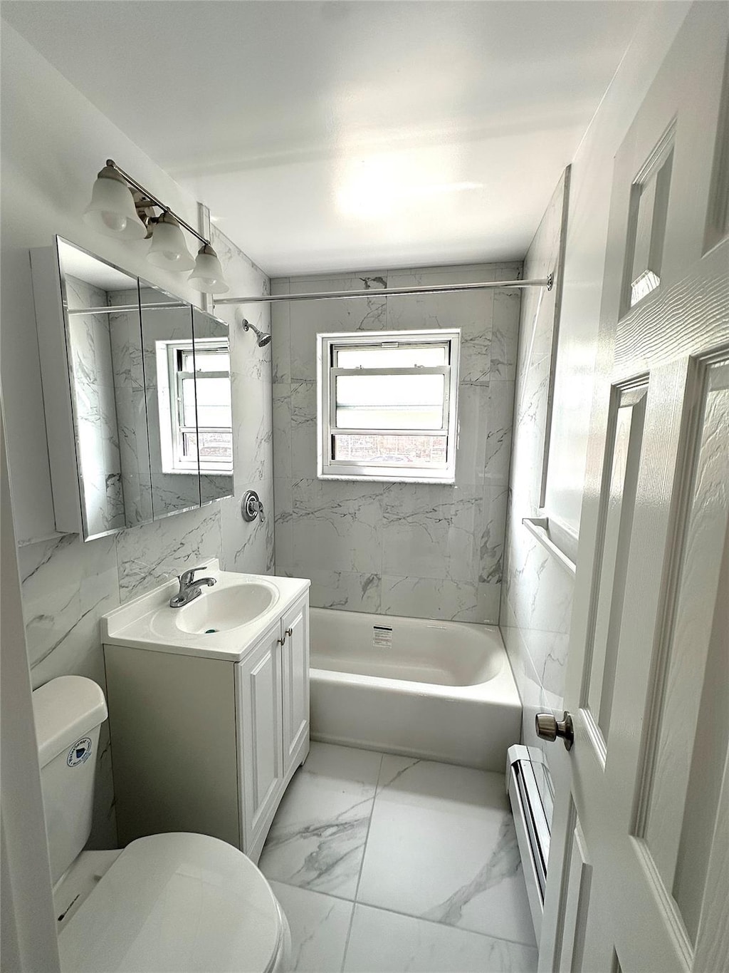 68-14 150th St Unit 463B, Flushing, NY 11367 - bathroom with a baseboard heating unit, toilet, vanity, washtub / shower combination, and plenty of natural light