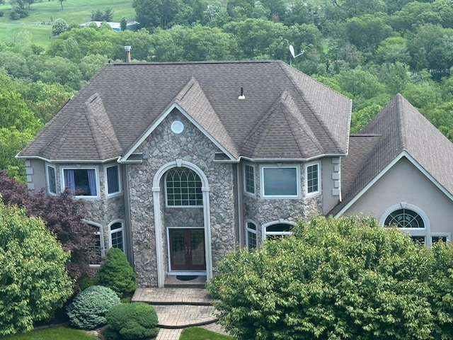 view of front of house with french doors, stone siding, and roof with shingles