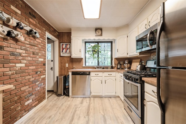 25 Cliffside Dr, Yonkers, NY 10710 - kitchen with stainless steel appliances, brick wall, healthy amount of natural light, light wood-type flooring, and white cabinetry