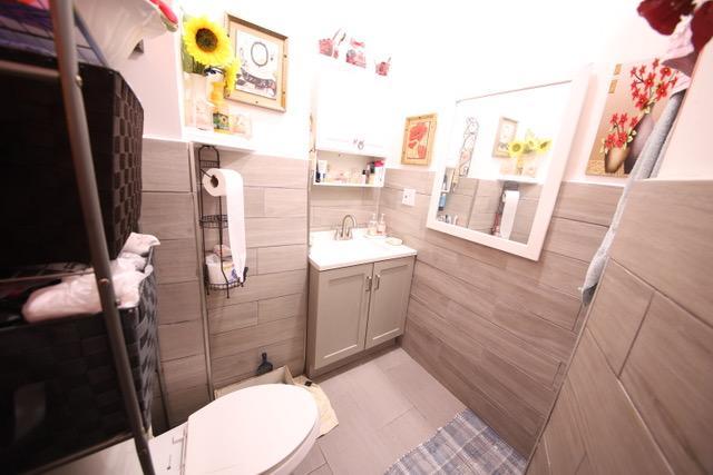 228 N 5th Ave, Mount Vernon, NY 10550 - bathroom with tile walls, vanity, toilet, wainscoting, and tile patterned flooring