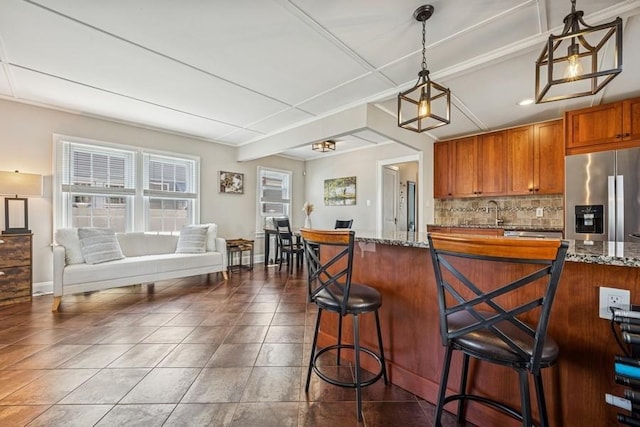 2660 Rosebud Ave, Merrick, NY 11566 - kitchen featuring stainless steel fridge, tasteful backsplash, brown cabinetry, dark stone countertops, and a kitchen bar