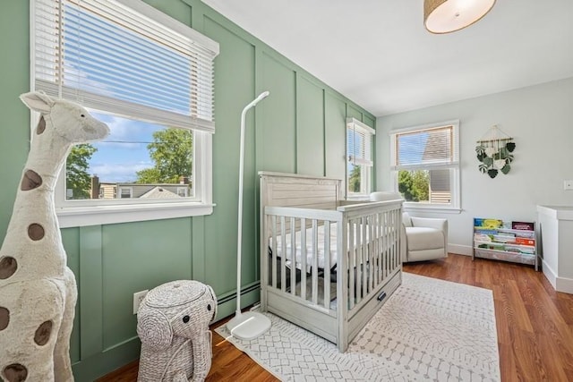 2660 Rosebud Ave, Merrick, NY 11566 - bedroom featuring a crib, wood finished floors, and baseboard heating