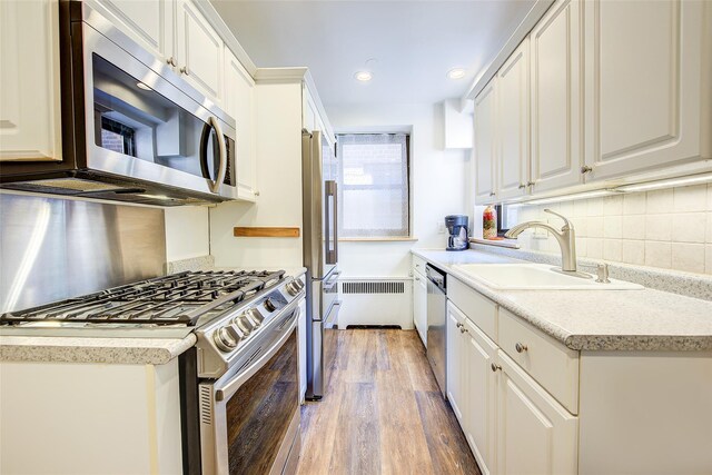 2 Town House Pl Unit 2H, Great Neck, NY 11021 - kitchen with stainless steel appliances, a sink, light wood finished floors, backsplash, and white cabinetry