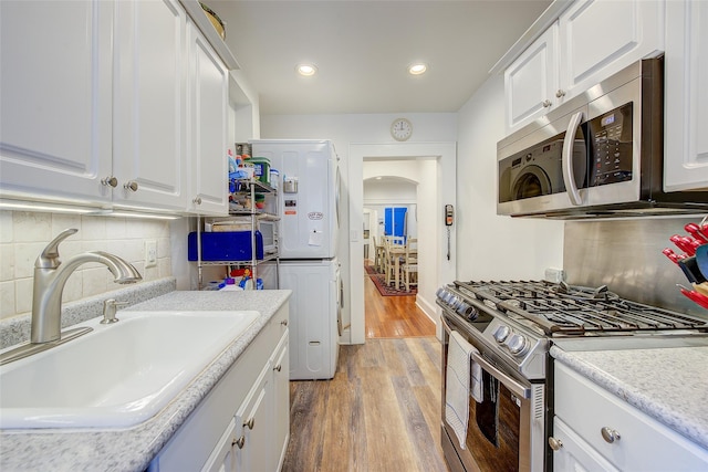 2 Town House Pl Unit 2H, Great Neck, NY 11021 - kitchen featuring stainless steel appliances, a sink, light wood-type flooring, decorative backsplash, and white cabinetry