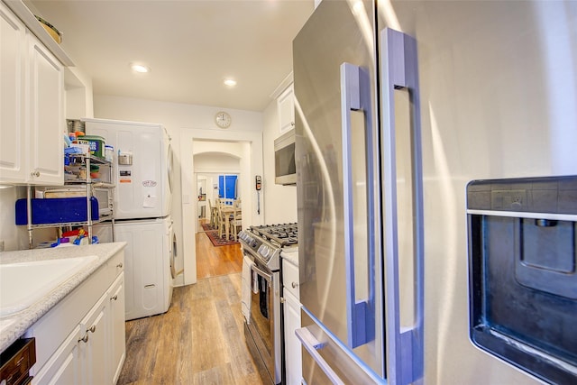 2 Town House Pl Unit 2H, Great Neck, NY 11021 - kitchen with stainless steel appliances, light wood finished floors, a sink, stacked washing machine and dryer, and white cabinets