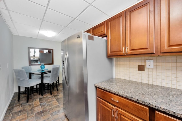 69-59 74th St, Middle Village, NY 11379 - kitchen featuring freestanding refrigerator, decorative backsplash, a paneled ceiling, stone finish floors, and brown cabinets