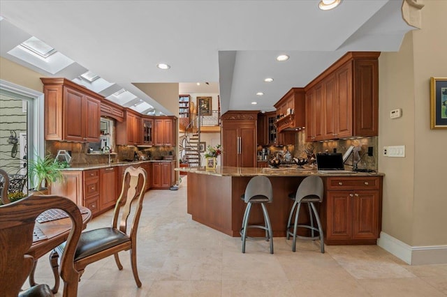 kitchen featuring a peninsula, light stone countertops, tasteful backsplash, glass insert cabinets, and recessed lighting