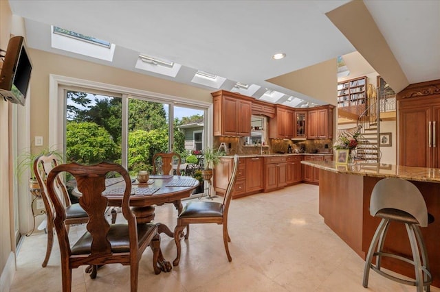 kitchen with brown cabinetry, light stone counters, decorative backsplash, a kitchen breakfast bar, and glass insert cabinets