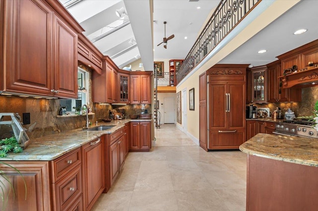 kitchen with a sink, stainless steel gas range oven, tasteful backsplash, light stone countertops, and vaulted ceiling