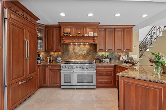 kitchen with high end appliances, light stone countertops, decorative backsplash, recessed lighting, and brown cabinets