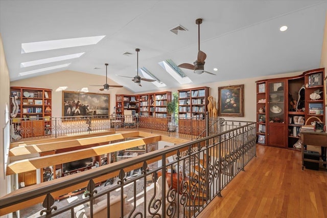 hallway with a skylight, lofted ceiling, wood finished floors, and an upstairs landing