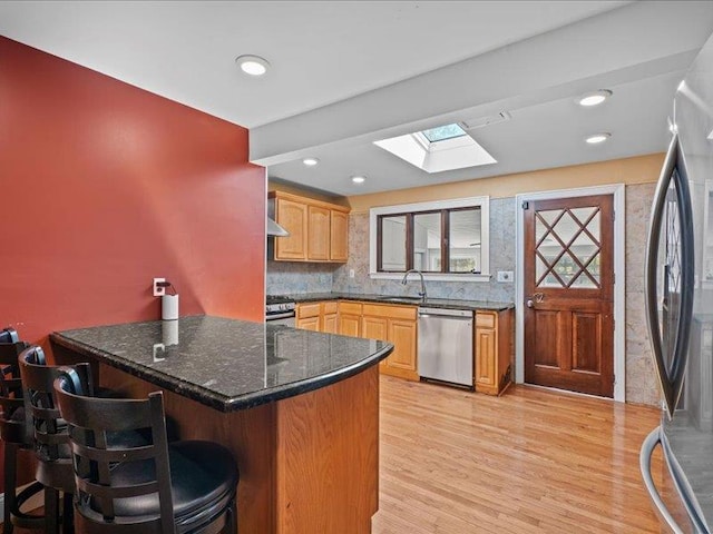 kitchen with stainless steel appliances, a skylight, a sink, a peninsula, and light wood-style floors