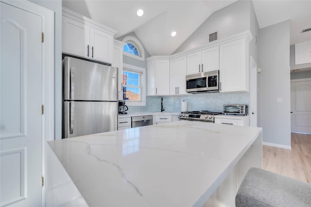 68 Brookline Ave, East Atlantic Beach, NY 11561 - kitchen featuring appliances with stainless steel finishes, white cabinets, decorative backsplash, light stone countertops, and lofted ceiling