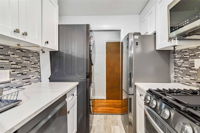 22-39 78th St Unit 2F, East Elmhurst, NY 11370 - kitchen with appliances with stainless steel finishes, backsplash, white cabinetry, light stone counters, and light wood-type flooring