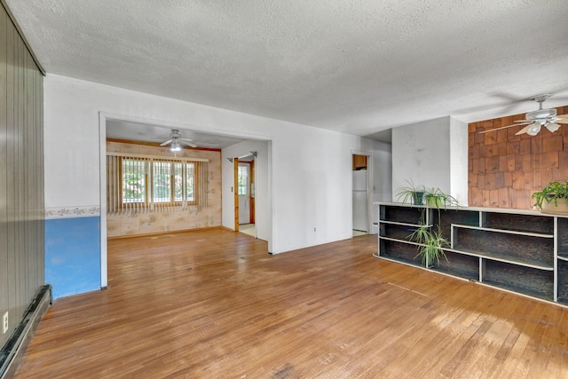 34 Leeside Dr, Carmel, NY 10512 - unfurnished living room featuring a baseboard radiator, a ceiling fan, wood finished floors, a textured ceiling, and wooden walls