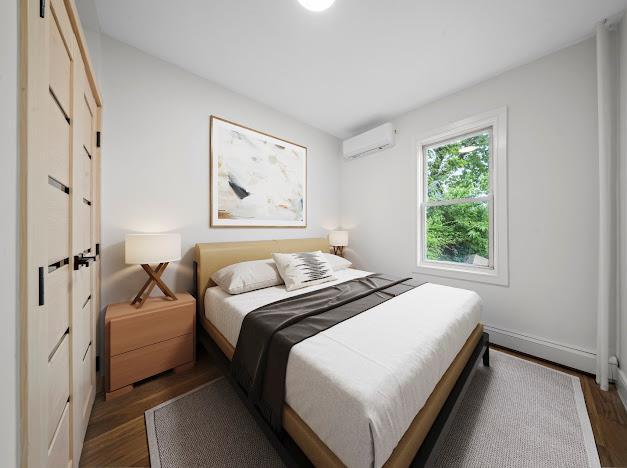 14-09 131st St, College Point, NY 11356 - bedroom with an AC wall unit, dark wood-style floors, and baseboards