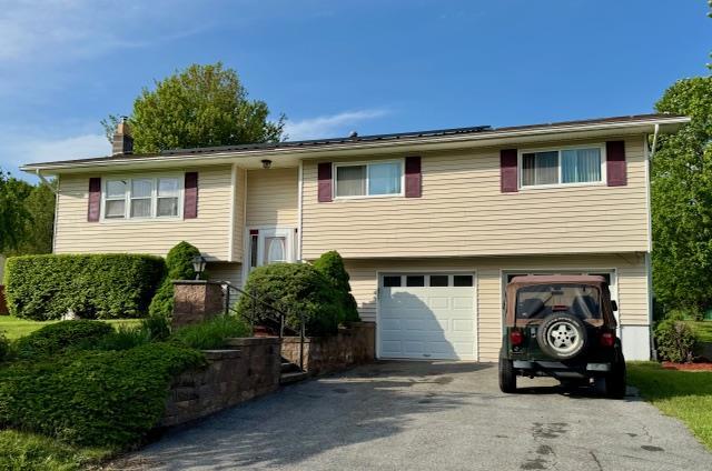 raised ranch featuring asphalt driveway, an attached garage, and a chimney