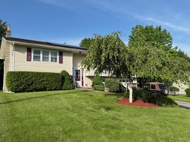 split foyer home with a front yard, roof mounted solar panels, and a chimney