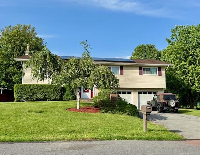 view of front facade with an attached garage, roof mounted solar panels, a front yard, and asphalt driveway