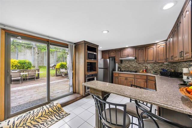 243 Sunflower Ln, Islandia, NY 11749 - kitchen with appliances with stainless steel finishes, light tile patterned flooring, backsplash, under cabinet range hood, and a peninsula