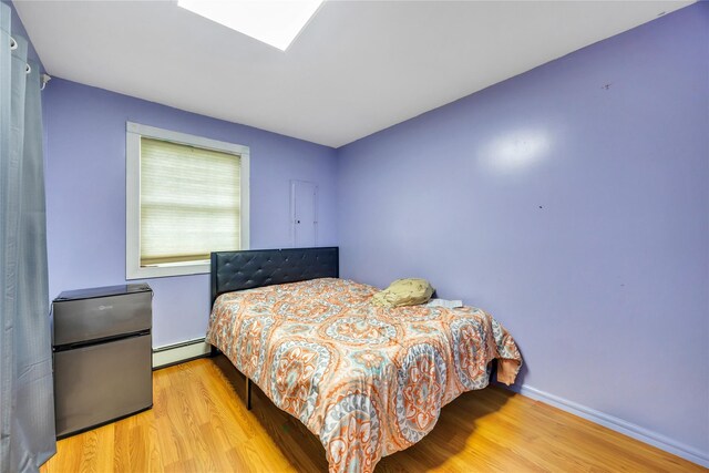 243 Sunflower Ln, Islandia, NY 11749 - bedroom featuring baseboard heating, wood finished floors, freestanding refrigerator, and baseboards
