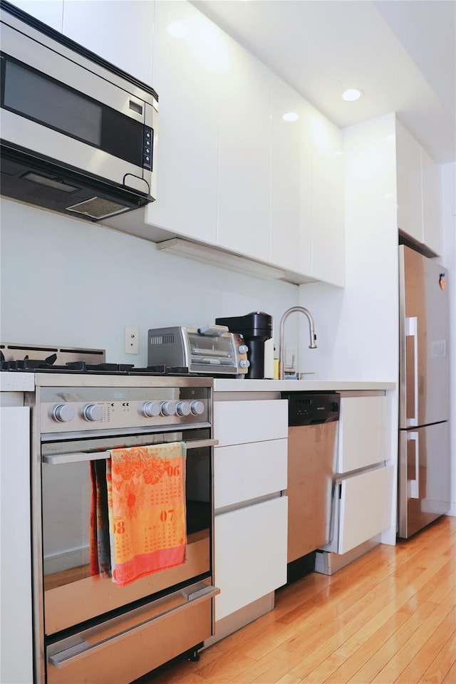 148 E 24th St Unit 5B, New York Manhattan, NY 10010 - kitchen with stainless steel appliances, white cabinetry, light wood finished floors, light countertops, and recessed lighting