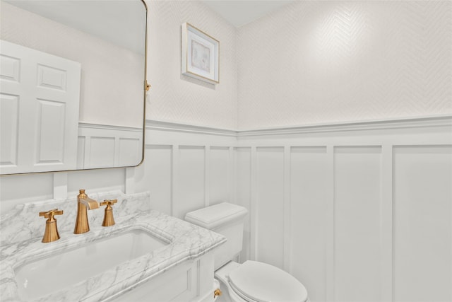 bathroom featuring a decorative wall, toilet, wainscoting, and vanity