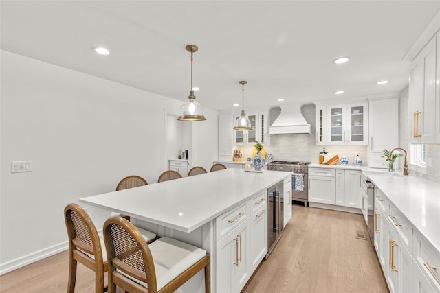 kitchen featuring custom range hood, high end stove, a sink, a kitchen breakfast bar, and backsplash