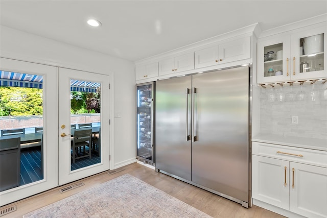 kitchen featuring stainless steel built in refrigerator, light wood finished floors, white cabinetry, tasteful backsplash, and glass insert cabinets