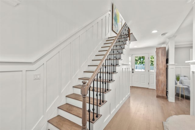 stairway featuring a decorative wall, wood finished floors, crown molding, and recessed lighting