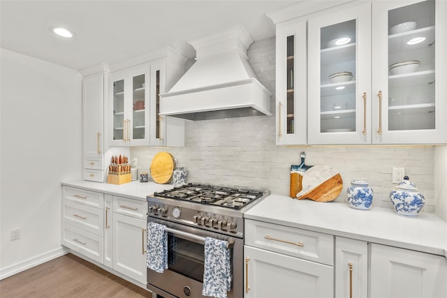 kitchen with stainless steel range, custom range hood, light countertops, light wood-style flooring, and white cabinets