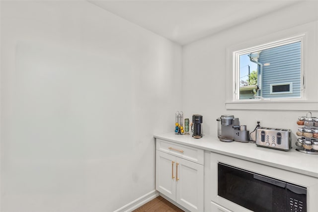 bar featuring built in microwave, baseboards, and light wood-style floors