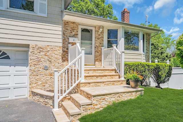view of exterior entry featuring a chimney, a yard, stone siding, a garage, and driveway