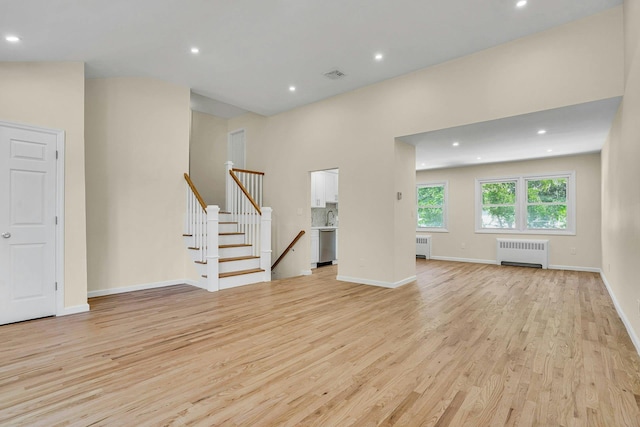 unfurnished living room with radiator heating unit, light wood-style flooring, recessed lighting, baseboards, and stairs