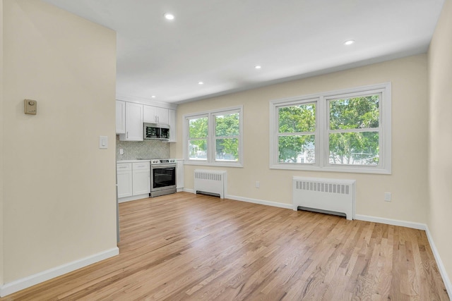 unfurnished living room with radiator heating unit, light wood-style floors, baseboards, and recessed lighting