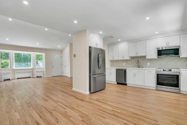 kitchen with stainless steel appliances, radiator heating unit, tasteful backsplash, light wood-style flooring, and recessed lighting