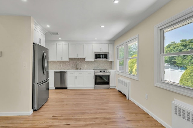 kitchen with appliances with stainless steel finishes, radiator heating unit, decorative backsplash, white cabinetry, and recessed lighting