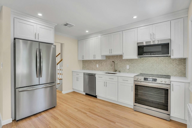 kitchen with stainless steel appliances, light countertops, tasteful backsplash, white cabinetry, and light wood-style flooring