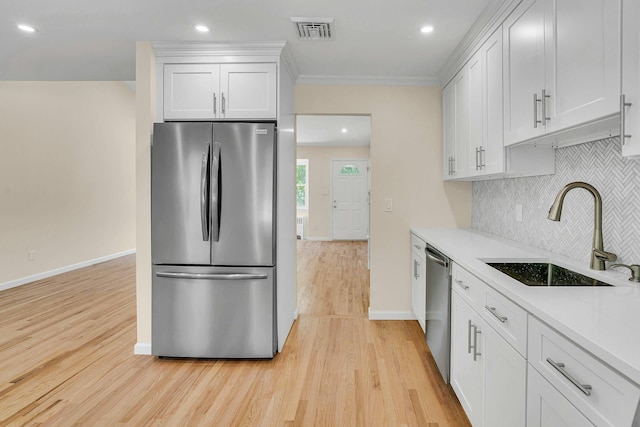 kitchen featuring appliances with stainless steel finishes, a sink, light wood-style floors, ornamental molding, and tasteful backsplash
