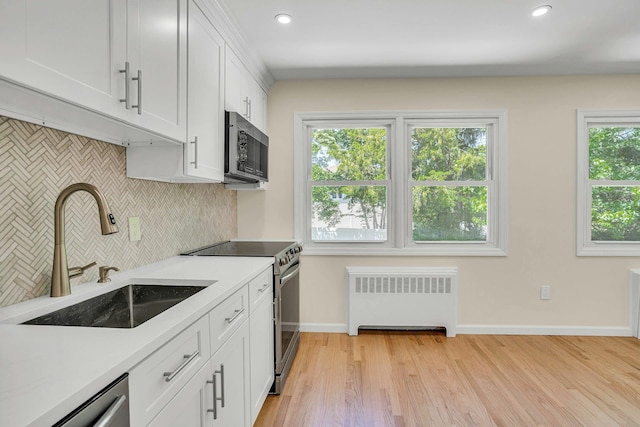 kitchen featuring radiator, appliances with stainless steel finishes, a sink, decorative backsplash, and baseboards